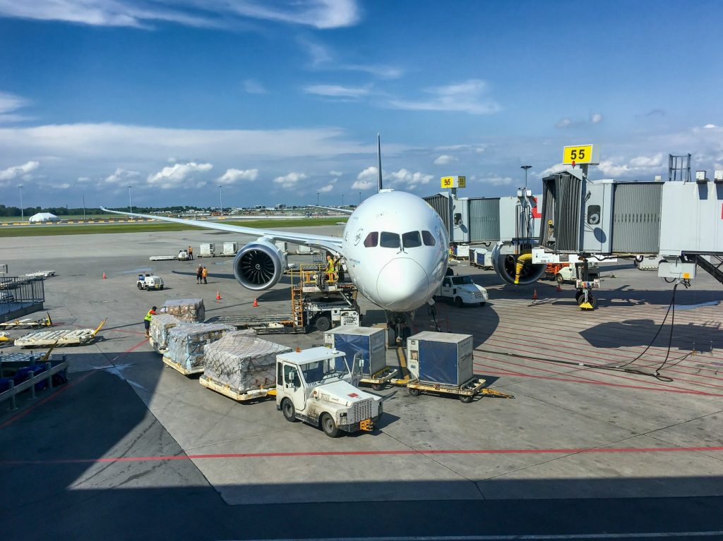 Passenger aircraft parked at an airport gate with a jet bridge, baggage carts, and ground service vehicles.